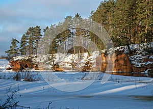 Winter landscape with red sandstone cliffs on the bank of the river Salaca, the sun shines on the trees and the river bank, the