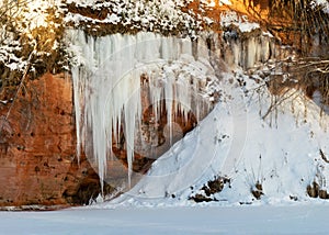 Winter landscape with red sandstone cliffs and icefall on the bank of the river Salaca, the sun shines on the trees and the bank
