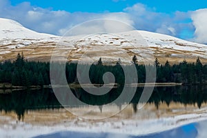 Winter landscape. Reflections in the reservoir of the Brecon Beacons with snow on the peaks of the mountains above.