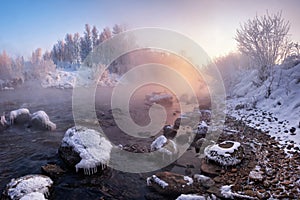 Winter Landscape: The River Flowing Among The Snow-Covered And Ice-Covered Stones And The Rose Sun Rising Over The Forest. Pinky W