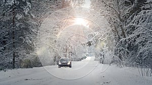 Winter landscape with road and mist. A car driving on a snowy road. The light of the setting sun shines through the branches of tr photo