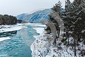 Winter landscape with rocks, stones and ice in the river in mountains. The trees and stones are covered with snow