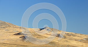 Winter landscape with a smooth hills covered with a yellow dry grass and first snow under dark blue sky