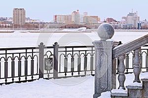 Winter landscape. Snow-covered embankment with granite balustrade railings. Black metal fence on a blurred background of