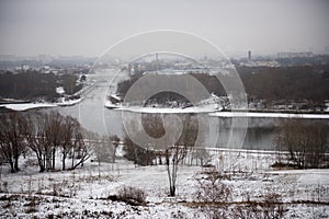 Winter landscape of snow-covered fields, trees and river in the early misty morning.