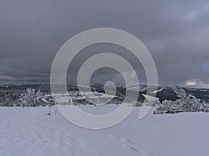 Winter landscape with snow-covered hiking path, frozen trees and view over Black Forest mountain range with pass road.