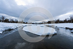 Winter landscape with snow covered lake and forest and mountains in the background.