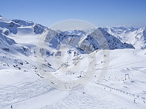 Winter landscape with snow covered mountain slopes and pistes with skiers enjoying spring sunny day at ski resort Stubai