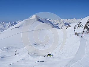 Winter landscape with snow covered mountain slopes and pistes with skiers enjoying spring sunny day at ski resort Stubai