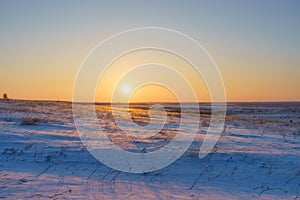 Winter landscape with snow covered plain, blue sky and orange sun at sunset. Beautiful natural scenic background