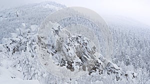 Winter landscape with snow covered rock cliff on slope. Coniferous forest after snowstorm