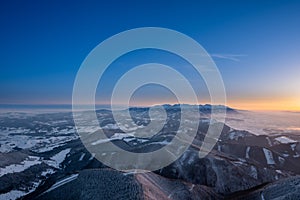 Winter landscape at sunrise from Velky Choc mountain in winter with fog in valley, view of low and high Tatras and Liptovska Mara