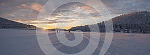 Winter landscape, sunset over snowy forest and frozen lake in Lapland. Trees covered with snow in the sun.