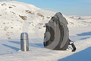 Winter landscape,thermos, and backpack are on the snow .