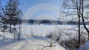 Winter landscape with trees on a cliff and a view from a height of a frozen river or a field with snow on a cold sunny