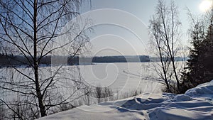 Winter landscape with trees on a cliff and a view from a height of a frozen river or a field with snow on a cold sunny