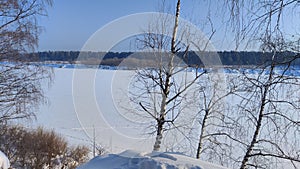 Winter landscape with trees on a cliff and a view from a height of a frozen river or a field with snow on a cold sunny