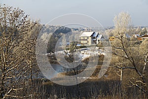 Winter landscape with a view of the lake, a rural house and a frost-covered forest in the distance