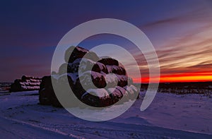 Winter landscape with view of snow-covered straw bales in field at sunset