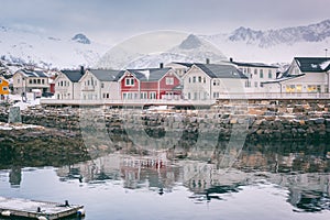 Winter landscape with white and red houses, reflection in the water and snowy mountain peaks, Kabelvag, Lofoten Islands, Norway