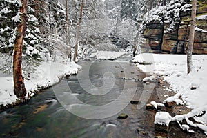 Winter landscape with white river, big rock in the background. Kamenice river, in Czech national park, Ceske Svycarsko, Bohemian S