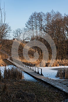 Winter landscape with a wooden bridge crossing a lake surrounded by reeds