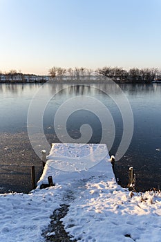 Winter landscape with wooden dock covered with snow above the frozen lake