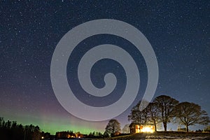 Winter landscape with wooden house under a beautiful starry sky and Northern Lights