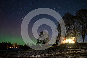 Winter landscape with wooden house under a beautiful starry sky and Northern Lights