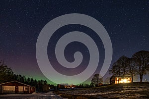 Winter landscape with wooden house under a beautiful starry sky and Northern Lights