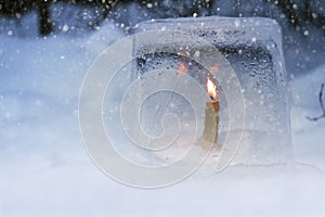 Winter lantern made of ice, burning candle inside, in snowfall