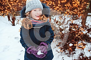 Winter lifestyle portrait of happy kid girl playing snowballs on the walk