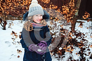 Winter lifestyle portrait of happy kid girl playing snowballs on the walk