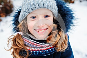 Winter lifestyle portrait of happy kid girl playing snowballs on the walk