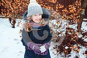 Winter lifestyle portrait of happy kid girl playing snowballs on the walk