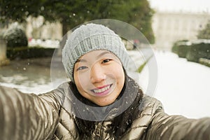 Winter lifestyle portrait of young happy and beautiful Asian Japanese woman taking selfie picture with mobile phone enjoying snow