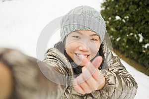 Winter lifestyle portrait of young happy and beautiful Asian Korean woman taking selfie picture with mobile phone enjoying snow at