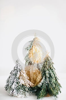 Winter magic forest, festive modern decor. Christmas little trees and golden lights bokeh on white background. Copy space.