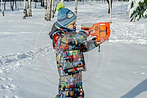 Winter morning, a boy in colorful clothes plays toy shoots in the snow