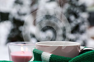 Winter morning. Cup with hot drink wrapped in green sweater and burning candle outdoors, closeup. Space for text