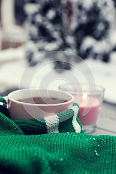 Winter morning. Cup with hot drink wrapped in green sweater and burning candle outdoors, closeup. Space for text