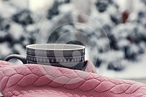Winter morning. Cup with hot drink wrapped in pink sweater outdoors, closeup. Space for text