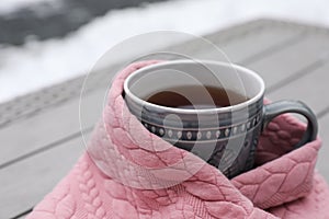 Winter morning. Cup with hot drink wrapped in pink sweater outdoors, closeup. Space for text