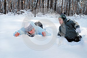 Winter mother with her son indulge lie on the snow in the forest