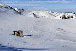 Winter mountain background with small wooden alpine cottage, on a snow field