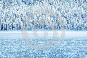 Winter mountain lake with snow-covered pine trees on the shore.