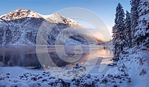 Winter mountain landscape. Beautiful ice lake in mountains. Scenery winter. Fir trees on snowy river shore. Wild nature landscape