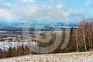 Winter mountain landscape with field, grove and village in far