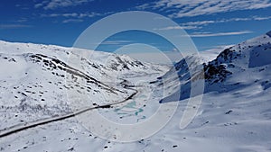 Winter mountain pass road cutting throught white winter landscape with vibrant blue lakes and tall mountain peaks on the Kaperdale