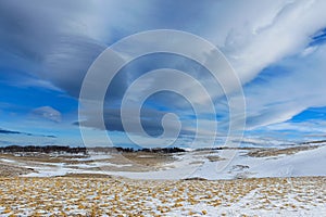 Winter mountain scenery. Beautiful unusual clouds in the blue sky. Below them is snow and yellow grass. A sunny, frosty